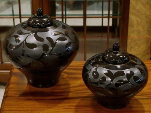 Czarny matowy wazon ceramiczny ze szkliwionym roślinnym dekorem zakończony czarnym dekoracyjnym wieczkiem.