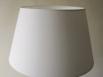 Biały stożkowy abażur dekoracyjnej lampy na komodę.